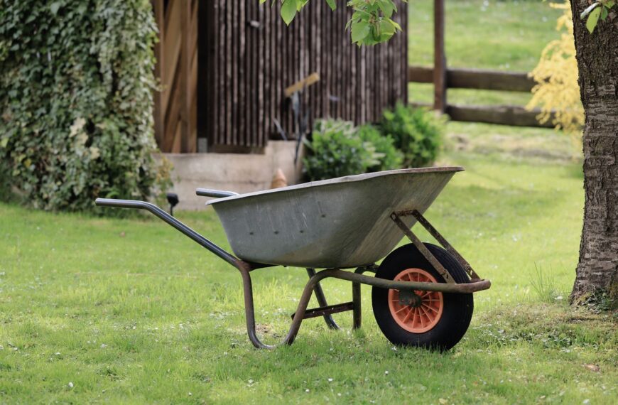A rustic wheelbarrow stands on green grass in a serene garden setting, ideal for gardening themes.