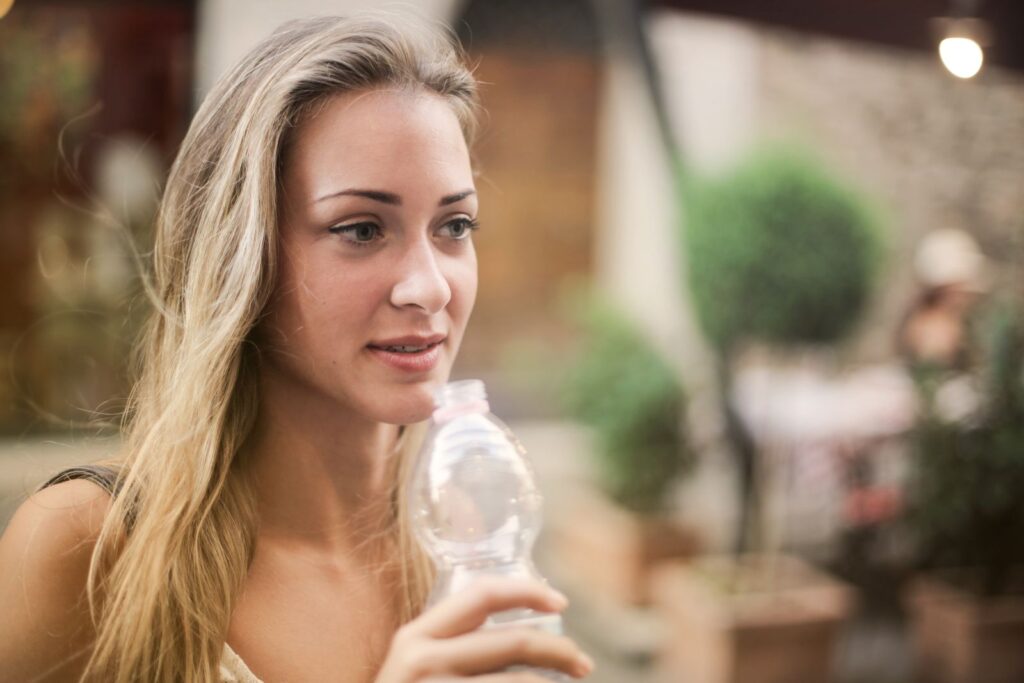 Serene female enjoying fresh water from plastic disposable bottle and strolling along city during weekend