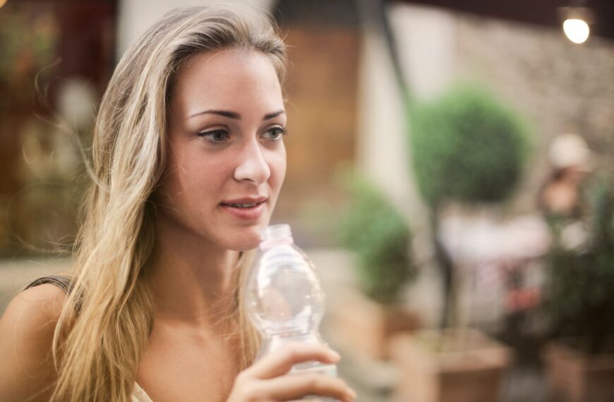 Serene female enjoying fresh water from plastic disposable bottle and strolling along city during weekend