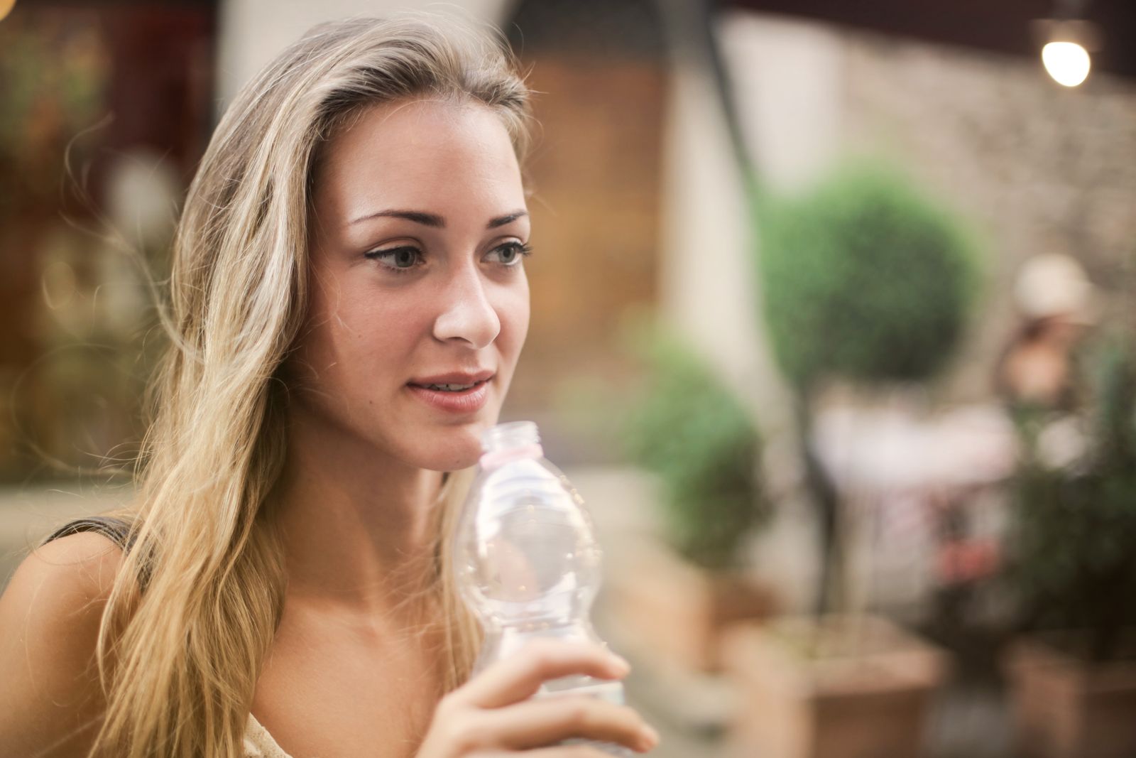 Serene female enjoying fresh water from plastic disposable bottle and strolling along city during weekend