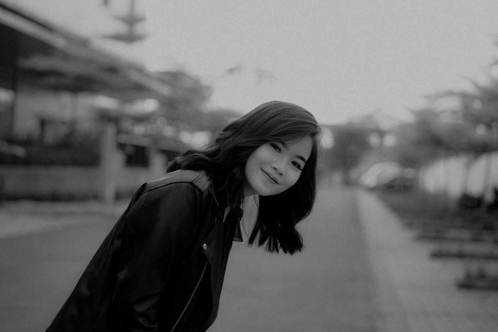 Black and white portrait of a smiling woman in an urban setting, exuding warmth and charm.