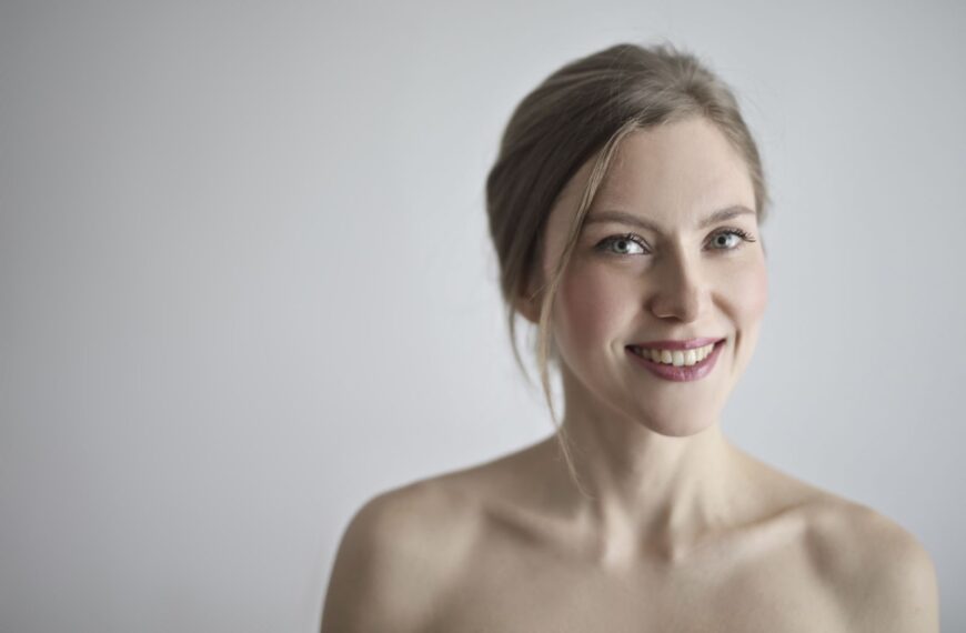 Close-up portrait of a smiling blonde woman against a gray background, embodying elegance and beauty.