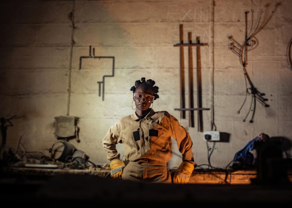 Confident female welder posing in a workshop with industrial tools and equipment.