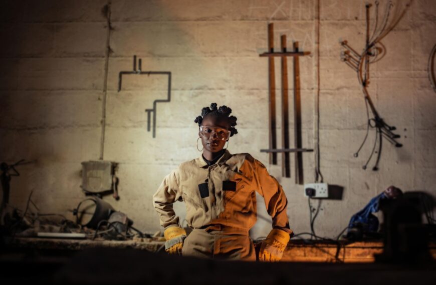Confident female welder posing in a workshop with industrial tools and equipment.