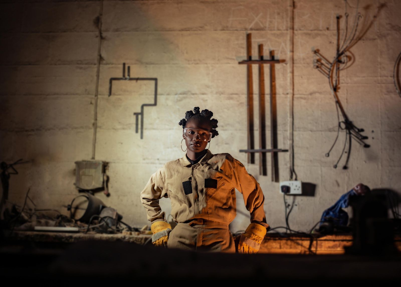 Confident female welder posing in a workshop with industrial tools and equipment.