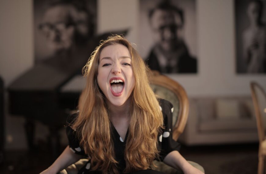 Portrait of a young woman with blonde hair expressing emotions while sitting indoors.
