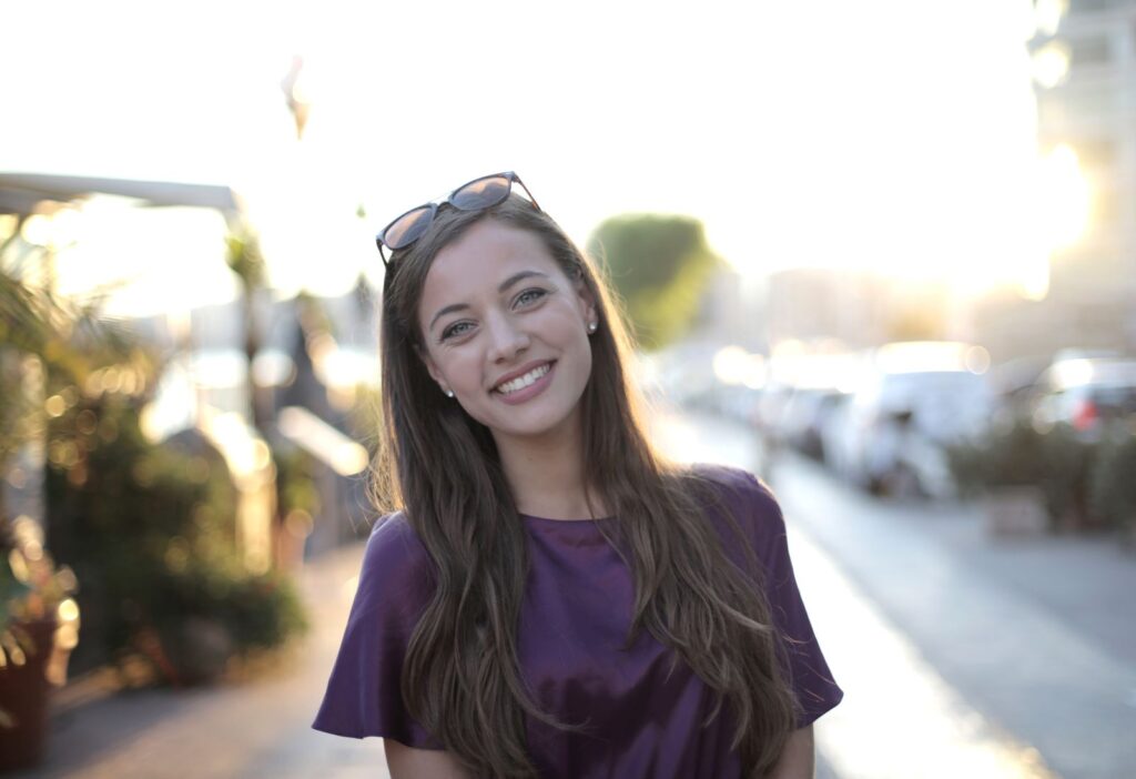Portrait of a smiling woman in sunlight on an urban street.