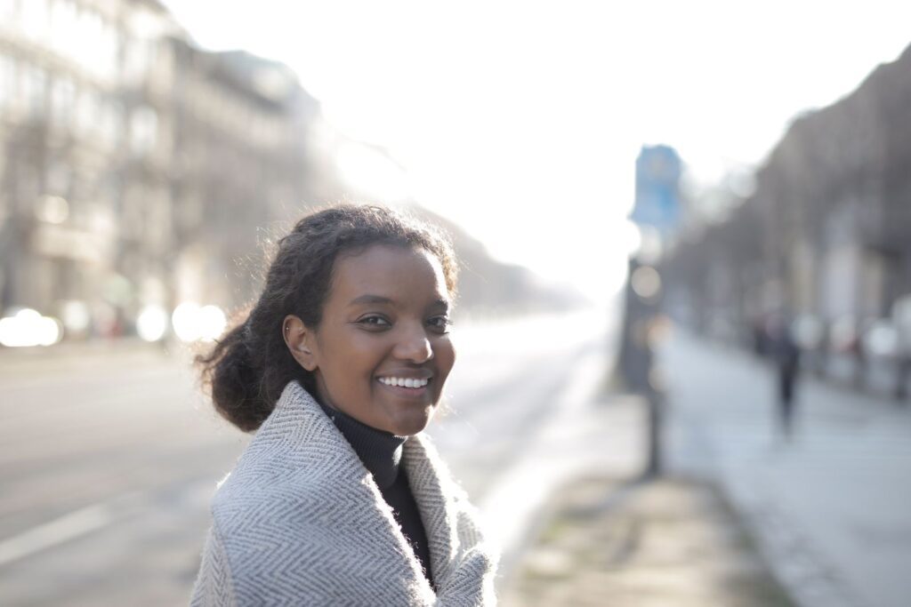 Joyful woman wearing a coat, smiling on a sunny day in the city.