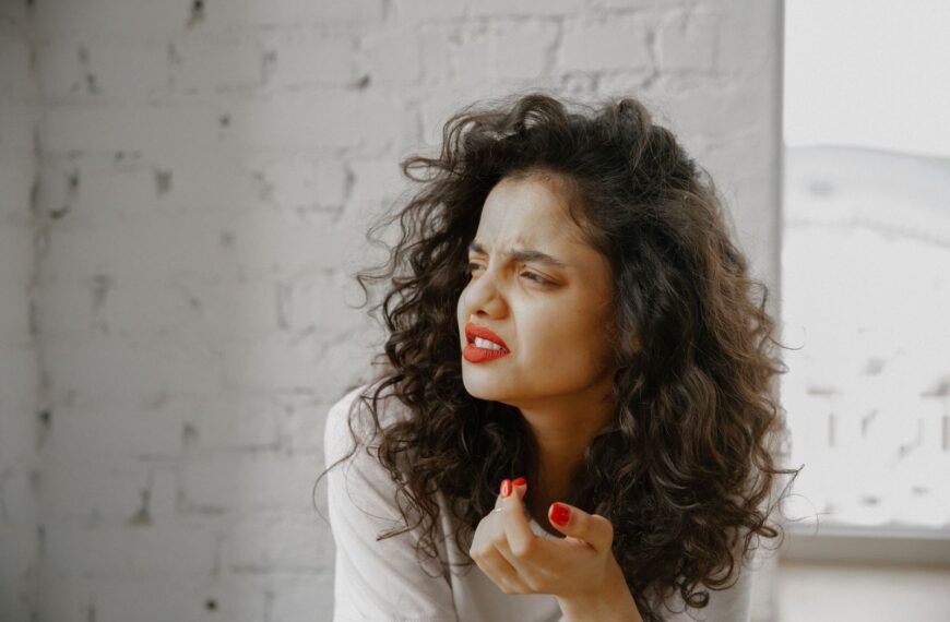 A brunette woman showing an expression of disgust against a brick wall.
