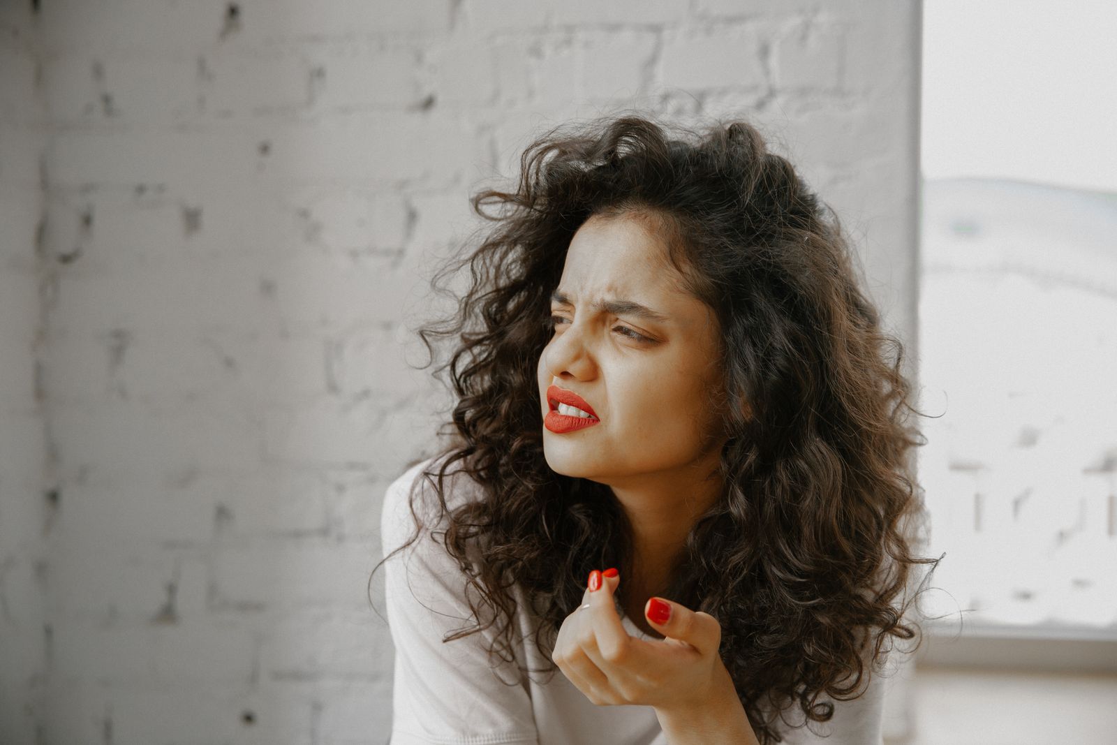 A brunette woman showing an expression of disgust against a brick wall.