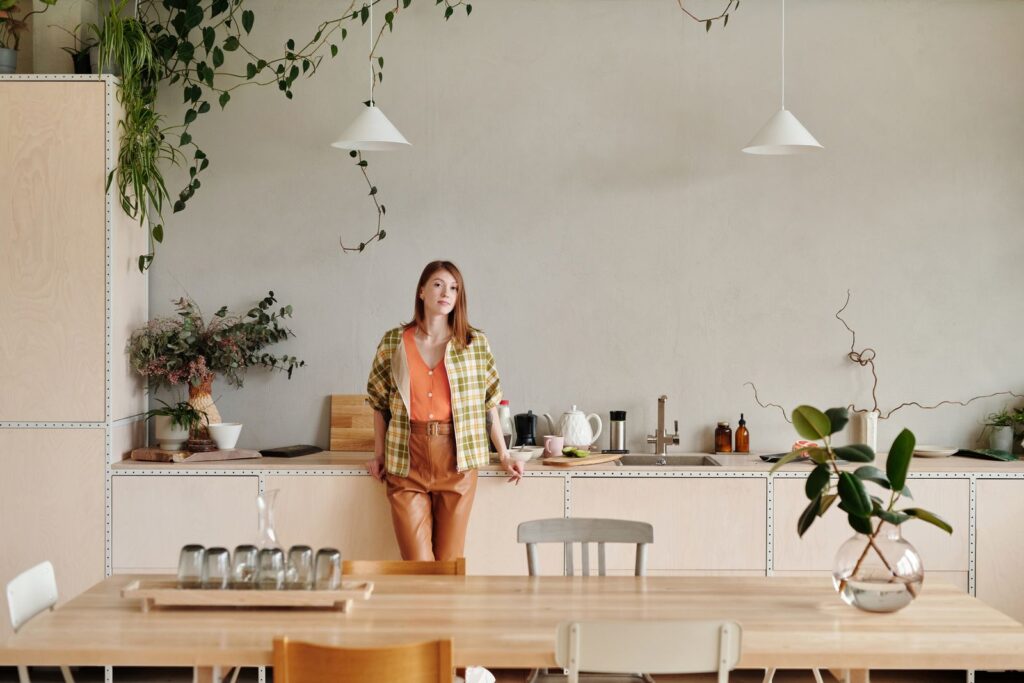 Modern kitchen with a stylish woman leaning on the counter, surrounded by plants.
