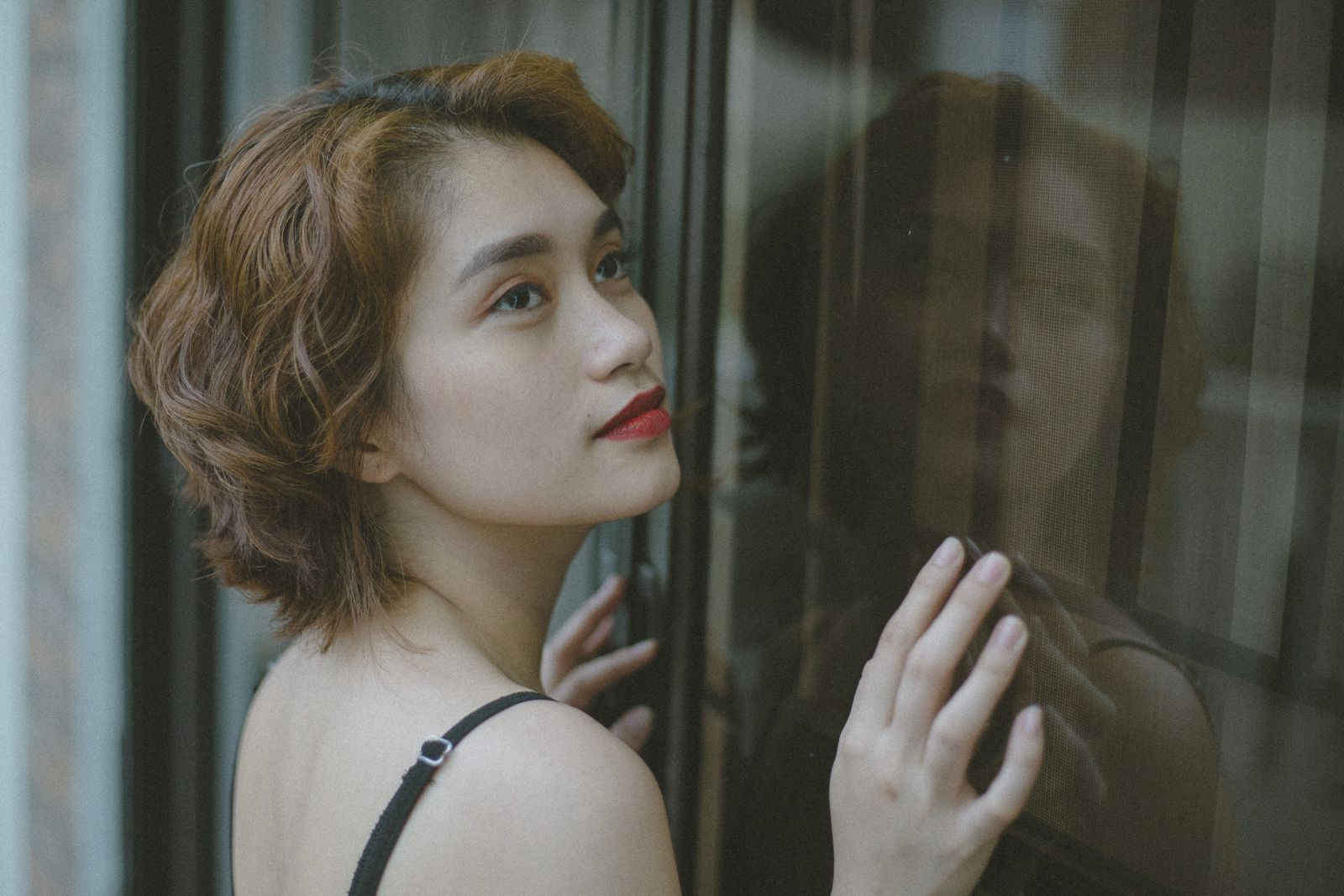A captivating portrait of an East Asian woman with red lips looking through a window, conveying elegance and introspection.