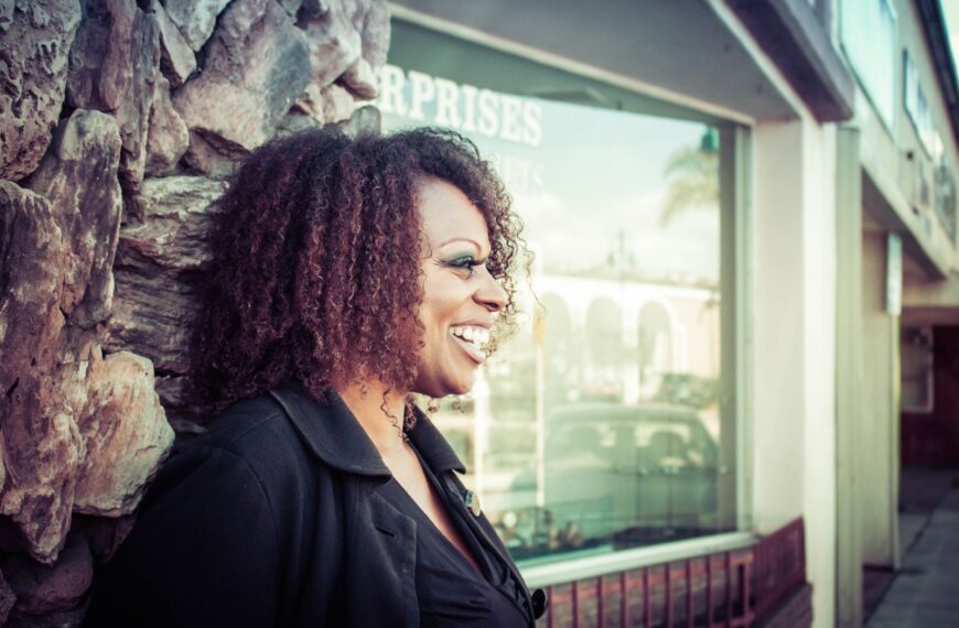 A smiling black woman enjoys a moment outside, embodying joy and urban style.