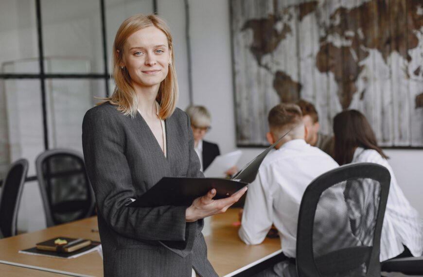 Confident businesswoman holding folder during a team meeting in modern office setting.