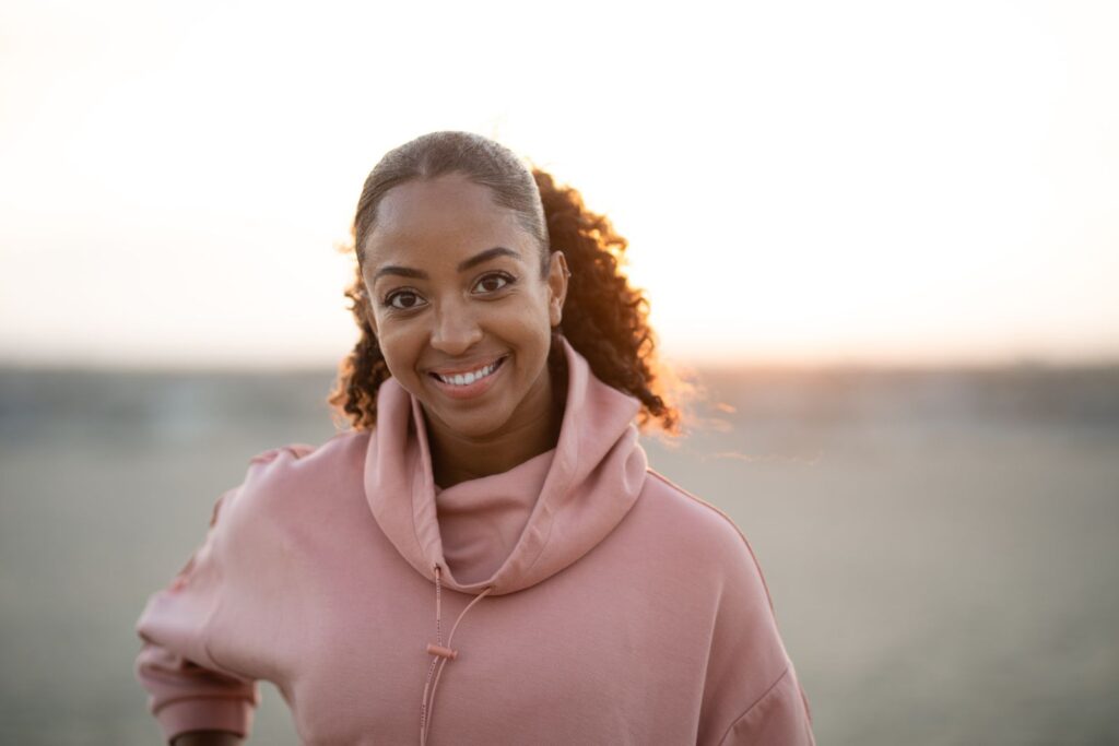 Cheerful woman in a pink hoodie enjoys a sunrise outdoors, exuding warmth and positivity.