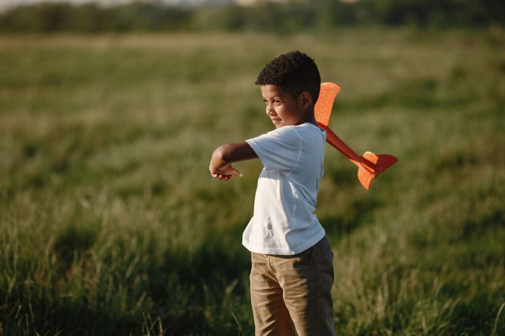 A child joyfully playing with a toy plane in a grassy meadow on a sunny day.