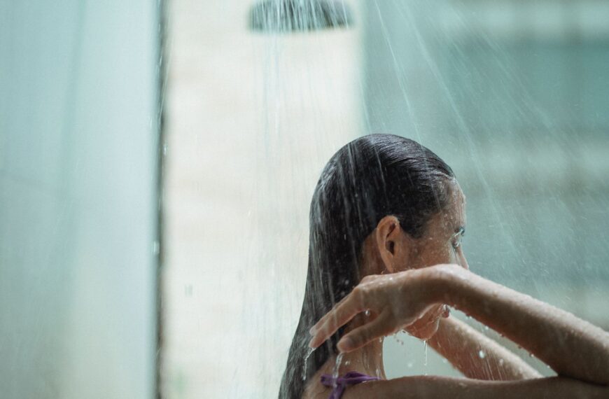 Side view of lady with closed eyes standing in shower and enjoying water