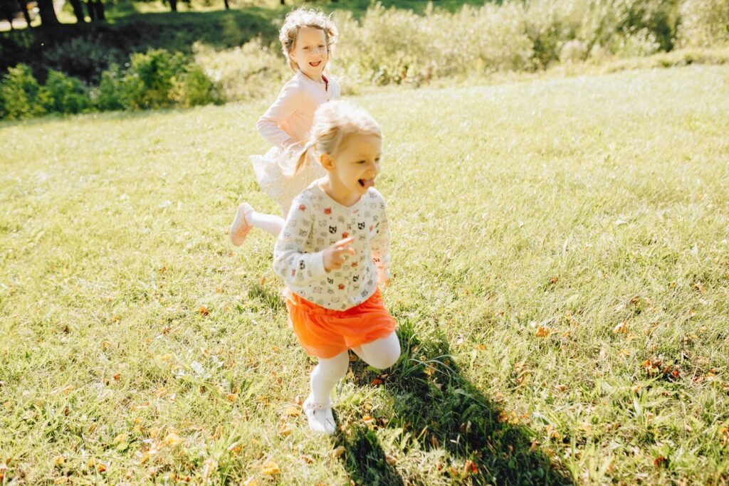 Two young girls laughing and playing on a sunny day in the park.