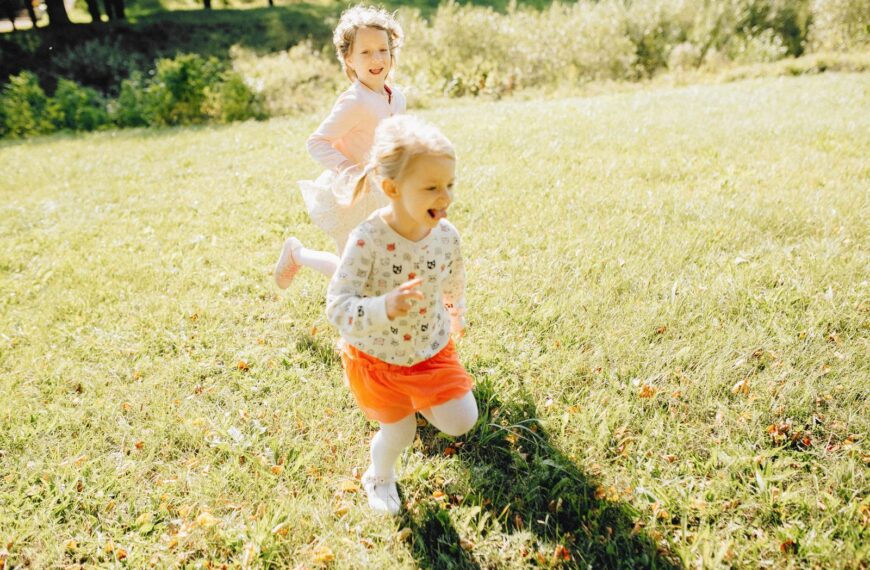 Two young girls laughing and playing on a sunny day in the park.