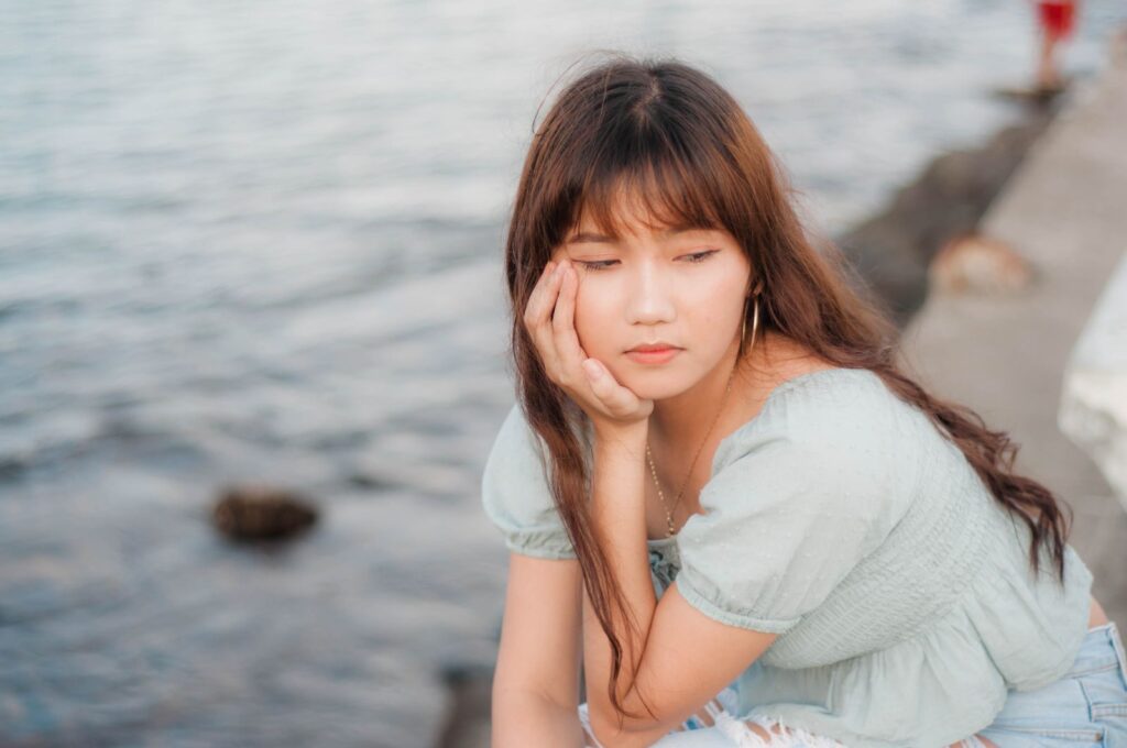 A thoughtful young woman sitting by the ocean, lost in deep reflection.