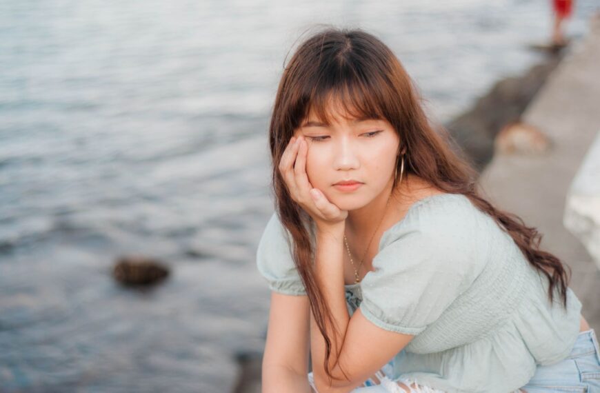 A thoughtful young woman sitting by the ocean, lost in deep reflection.