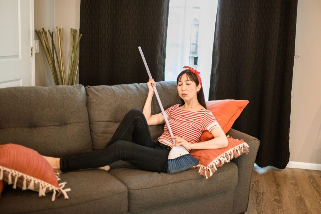 Woman lounging on a sofa holding a broom, in a cozy indoor setting.
