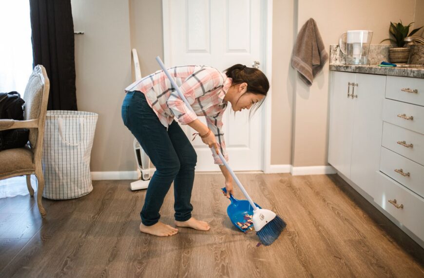 An Asian woman performing cleaning chores by sweeping the floor indoors.