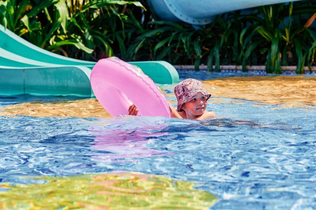 A child playing with a pink floater in a swimming pool on a sunny day.