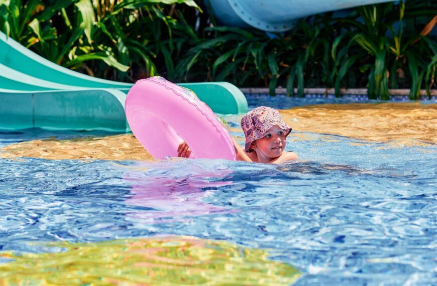 A child playing with a pink floater in a swimming pool on a sunny day.