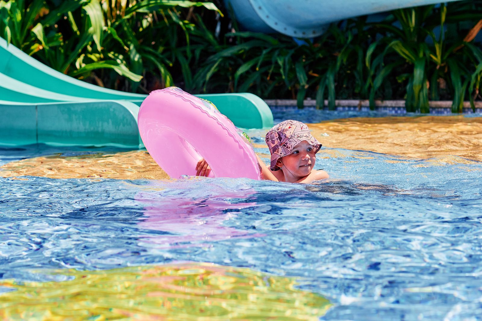 A child playing with a pink floater in a swimming pool on a sunny day.