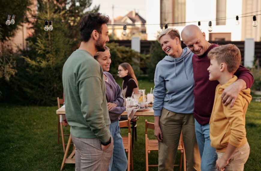 Happy family in casual clothes laughing and having picnic in backyard with string of light bulbs in daytime
