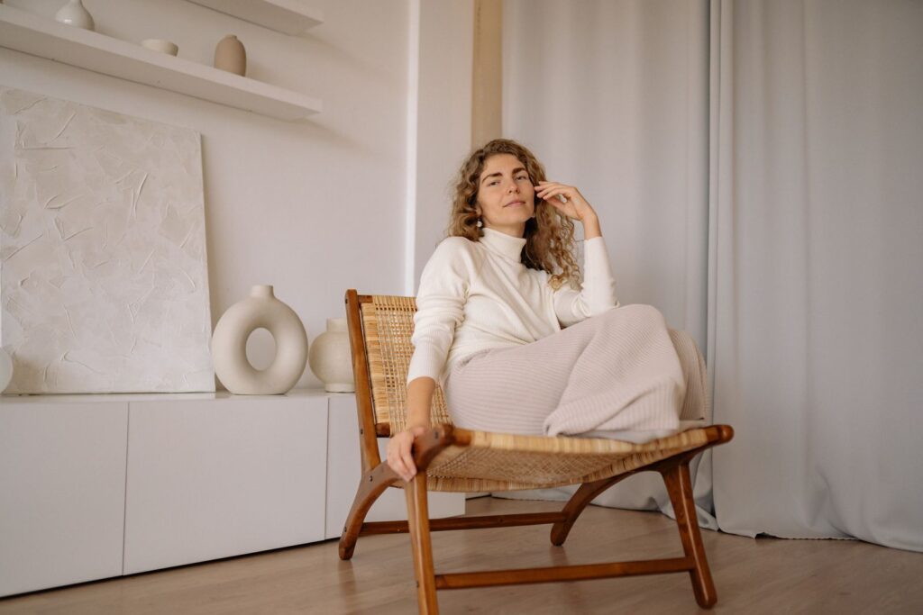 A woman relaxing in a wicker chair indoors with a minimalist background.