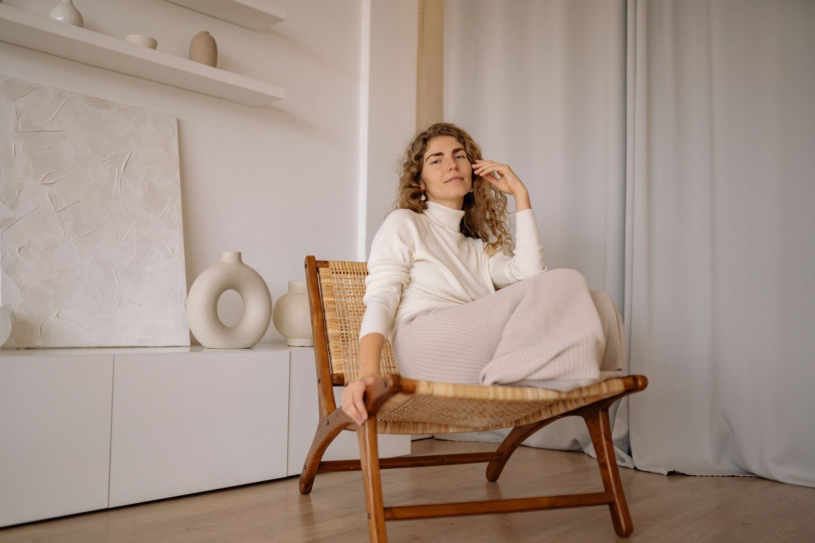 A woman relaxing in a wicker chair indoors with a minimalist background.