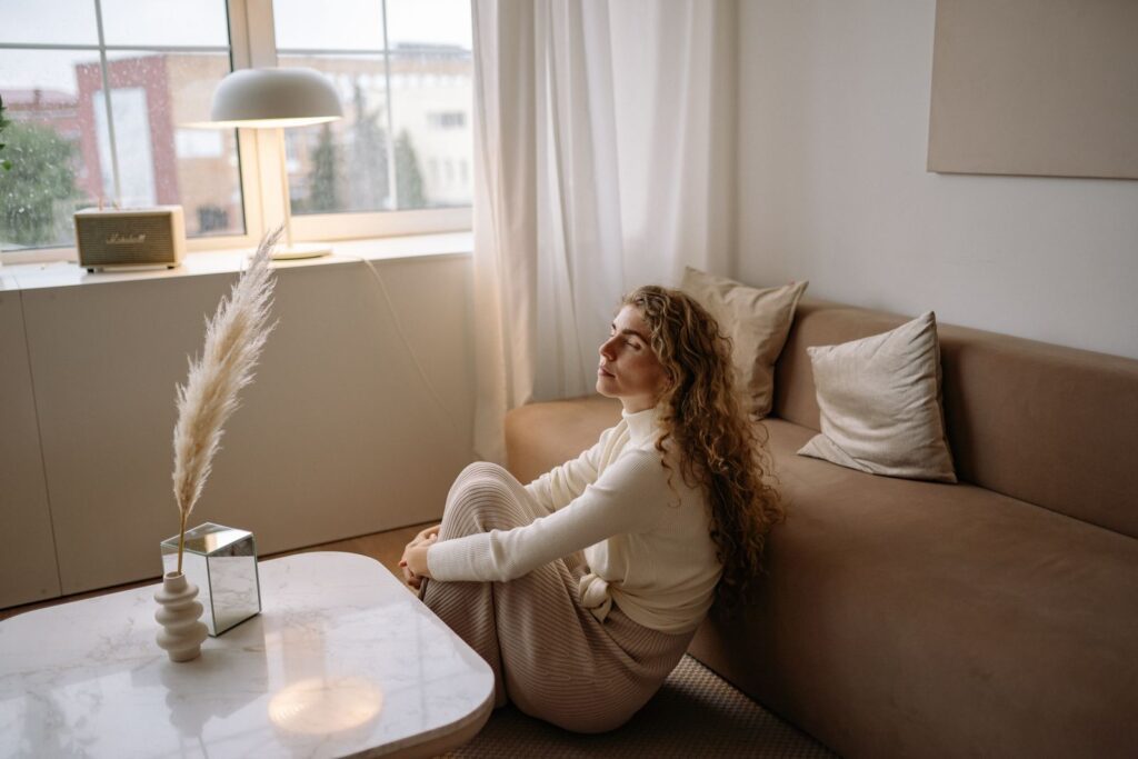 A woman sitting on a sofa in a calm, minimalist living room setting.
