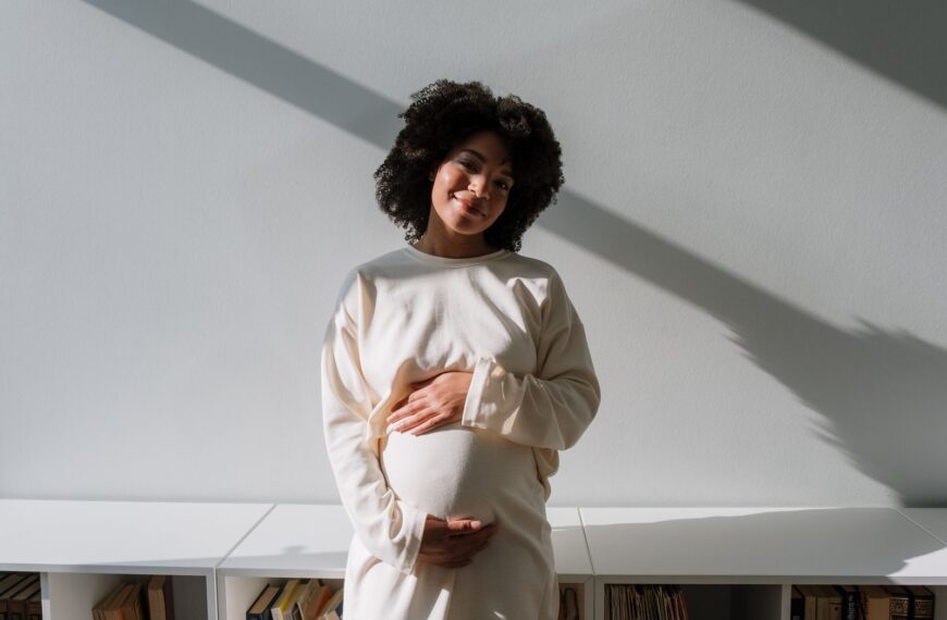 Beautiful pregnant woman with curly hair embracing maternity in a serene indoor setting.
