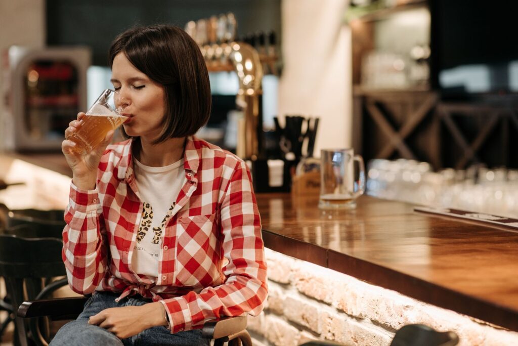 Woman sipping craft beer at a cozy pub, showcasing leisure and relaxation indoors.
