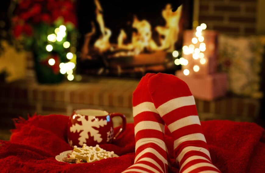 Warm holiday scene with striped socks, a mug, and cookies by a fireplace.