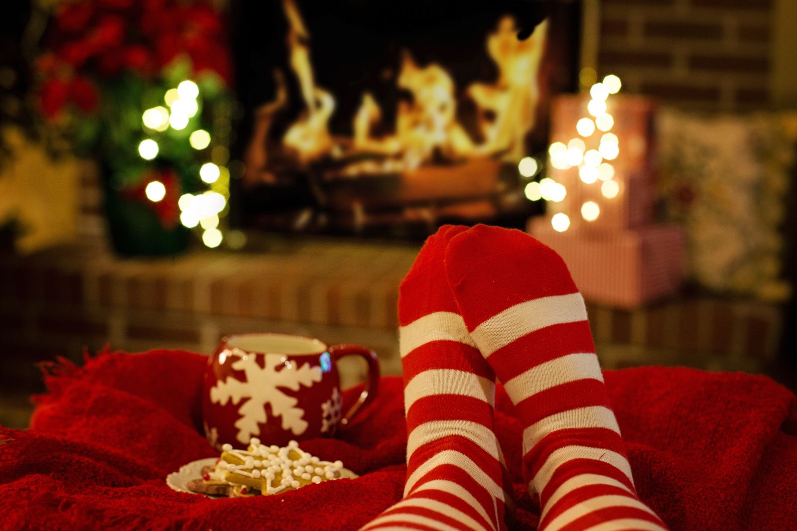 Warm holiday scene with striped socks, a mug, and cookies by a fireplace.