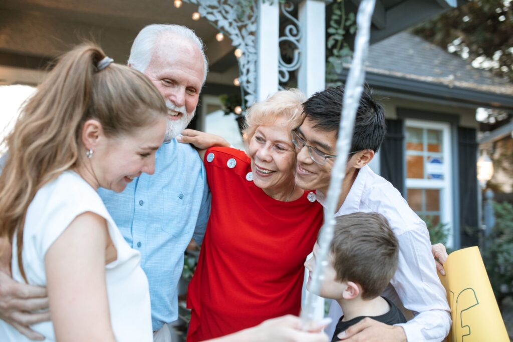 A joyful multigenerational family gathering, embracing each other outdoors with happiness.