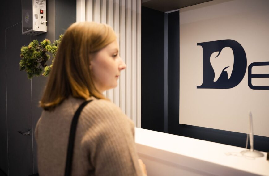 Young woman stands at a dental office reception, side view, casual attire.