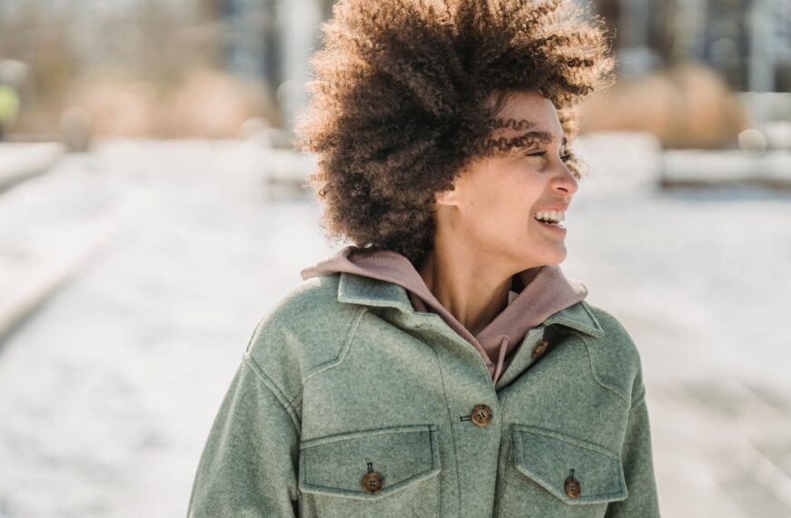 Laughing ethnic woman with dark curly hair in warm outerwear looking away while strolling outdoors in wintertime
