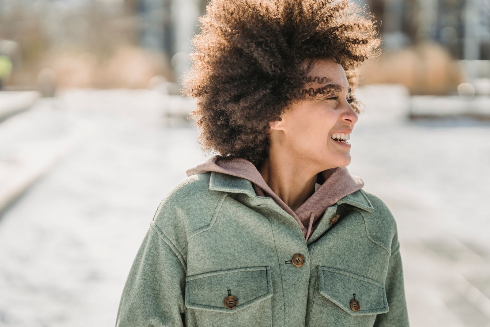 Laughing ethnic woman with dark curly hair in warm outerwear looking away while strolling outdoors in wintertime
