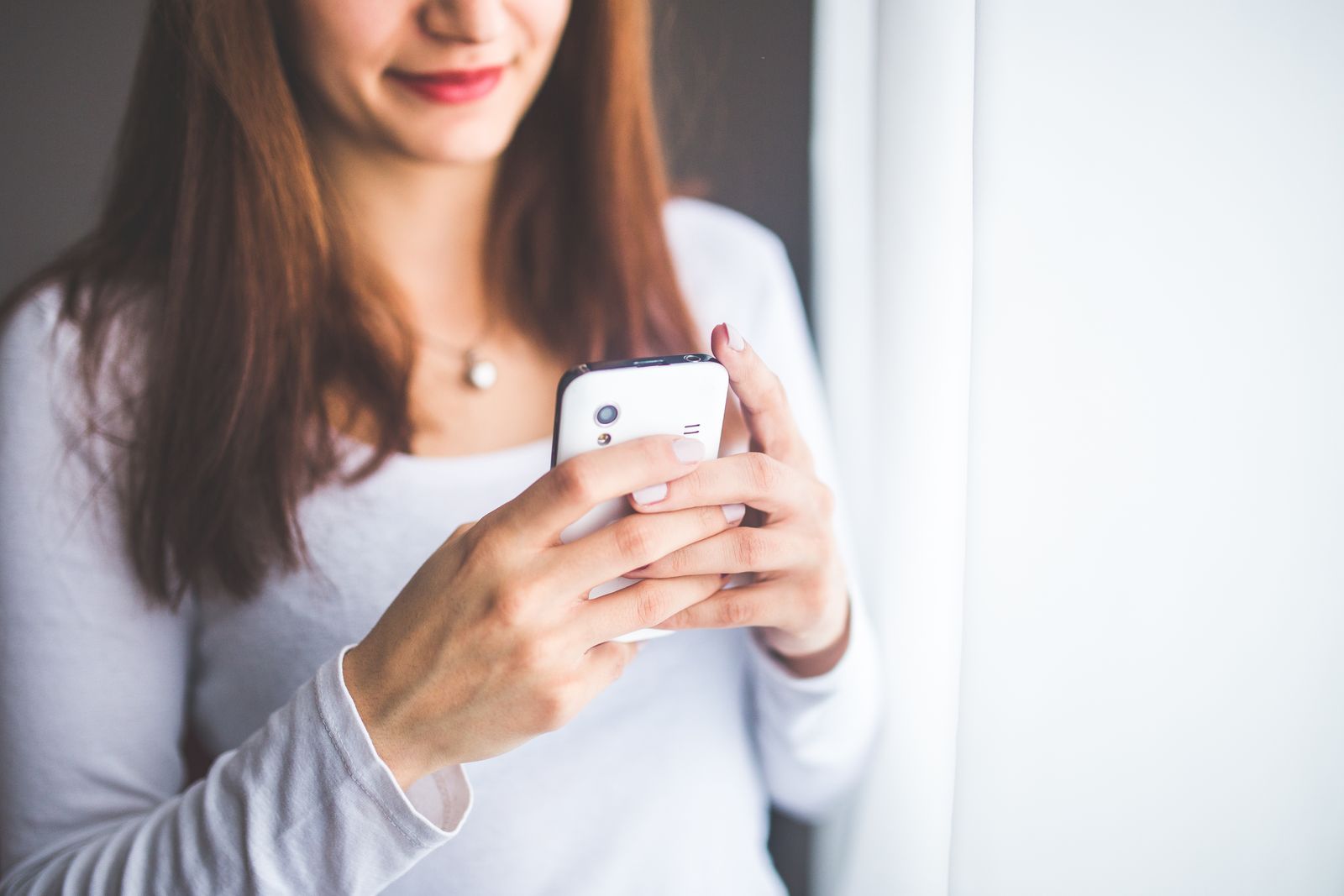 Young woman interacting with a smartphone near a window, showcasing modern communication technology.