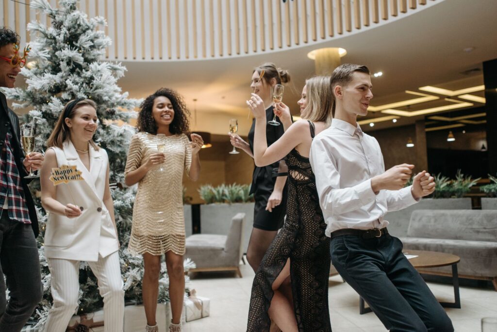 Group of adults enjoying a New Year's party indoors, dancing and holding champagne glasses.