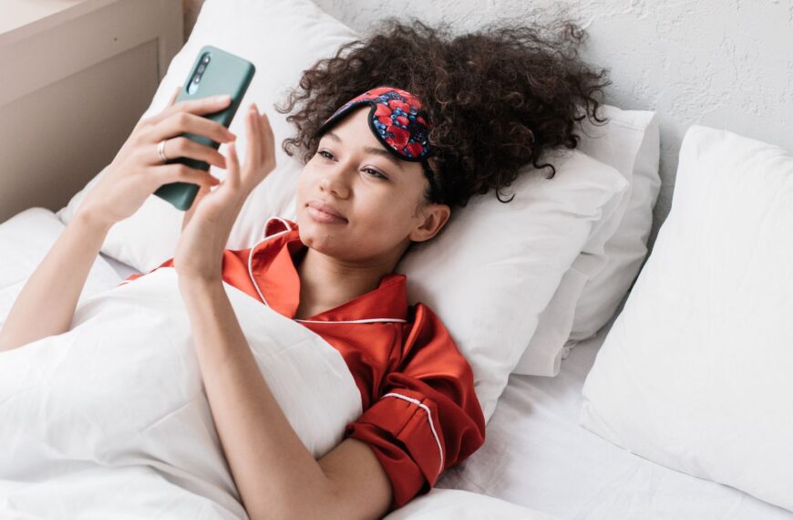 A woman in red pajamas using her smartphone while lying in bed.