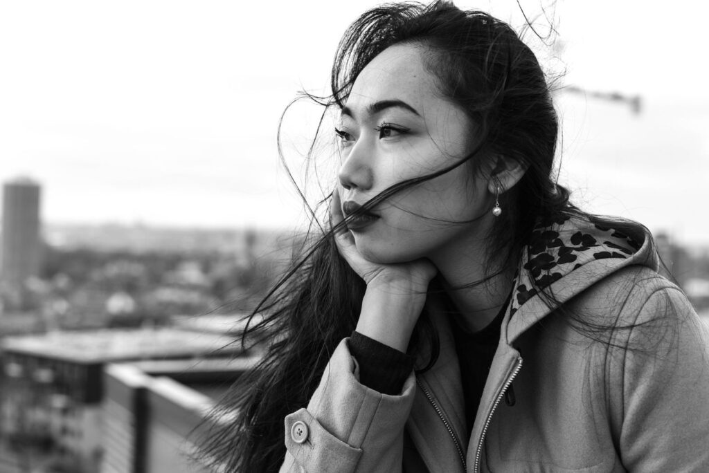 Woman with tousled hair gazing thoughtfully over a cityscape in black and white.