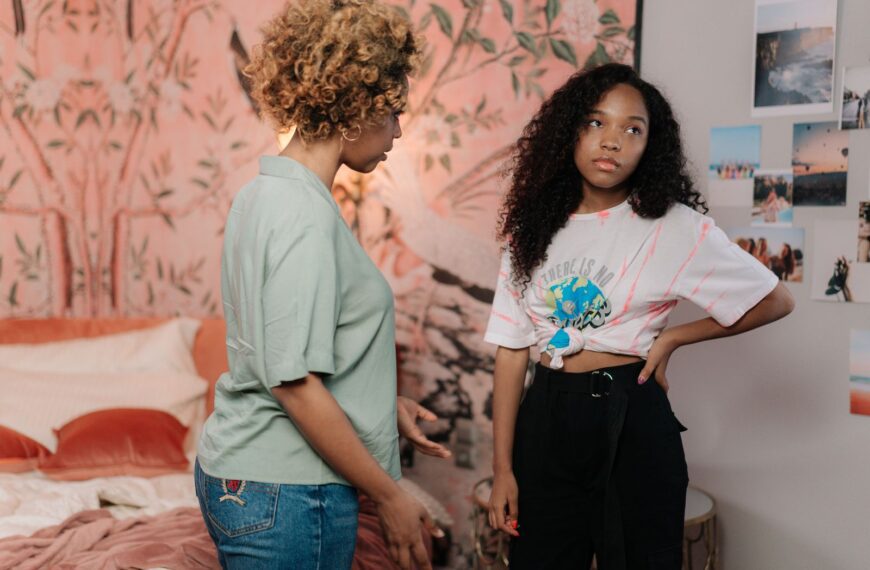 A mother and teen daughter in a tense conversation in a modern bedroom setting.