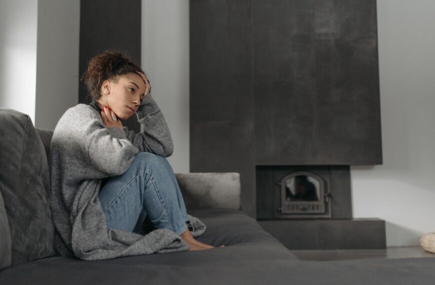 A woman in a cozy living room feeling unwell, sitting on a sofa with a thoughtful expression.