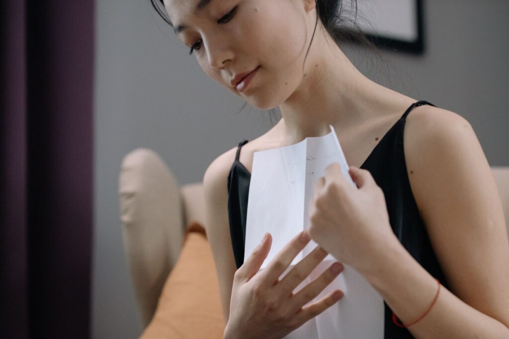 A contemplative woman holding a paper close to her heart in an indoor setting.