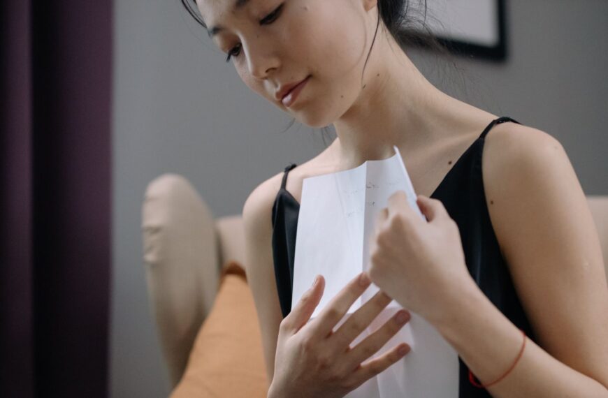 A contemplative woman holding a paper close to her heart in an indoor setting.